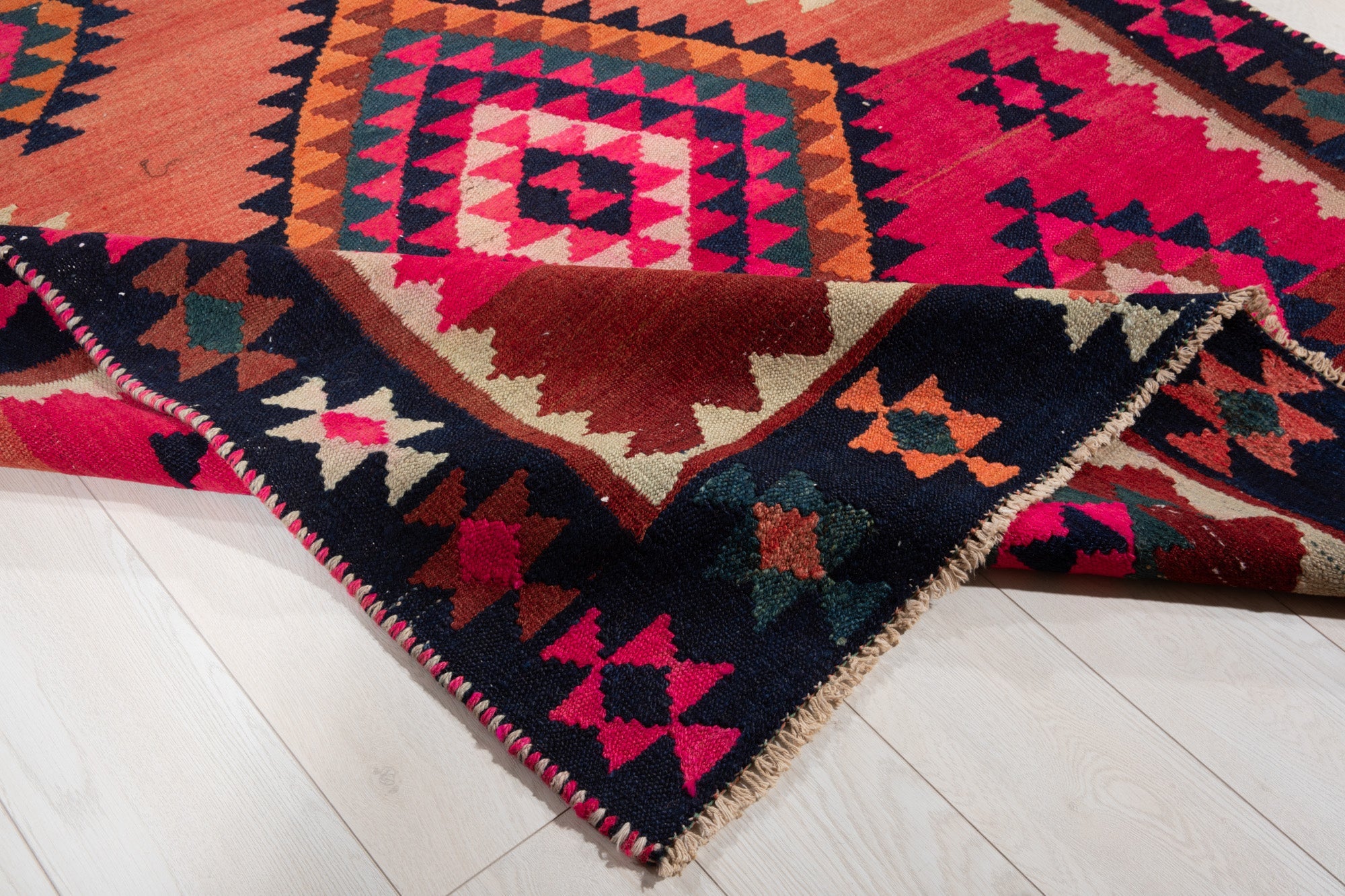 Corner of the kilim rug folded up, showing its border pattern and fringed edge.