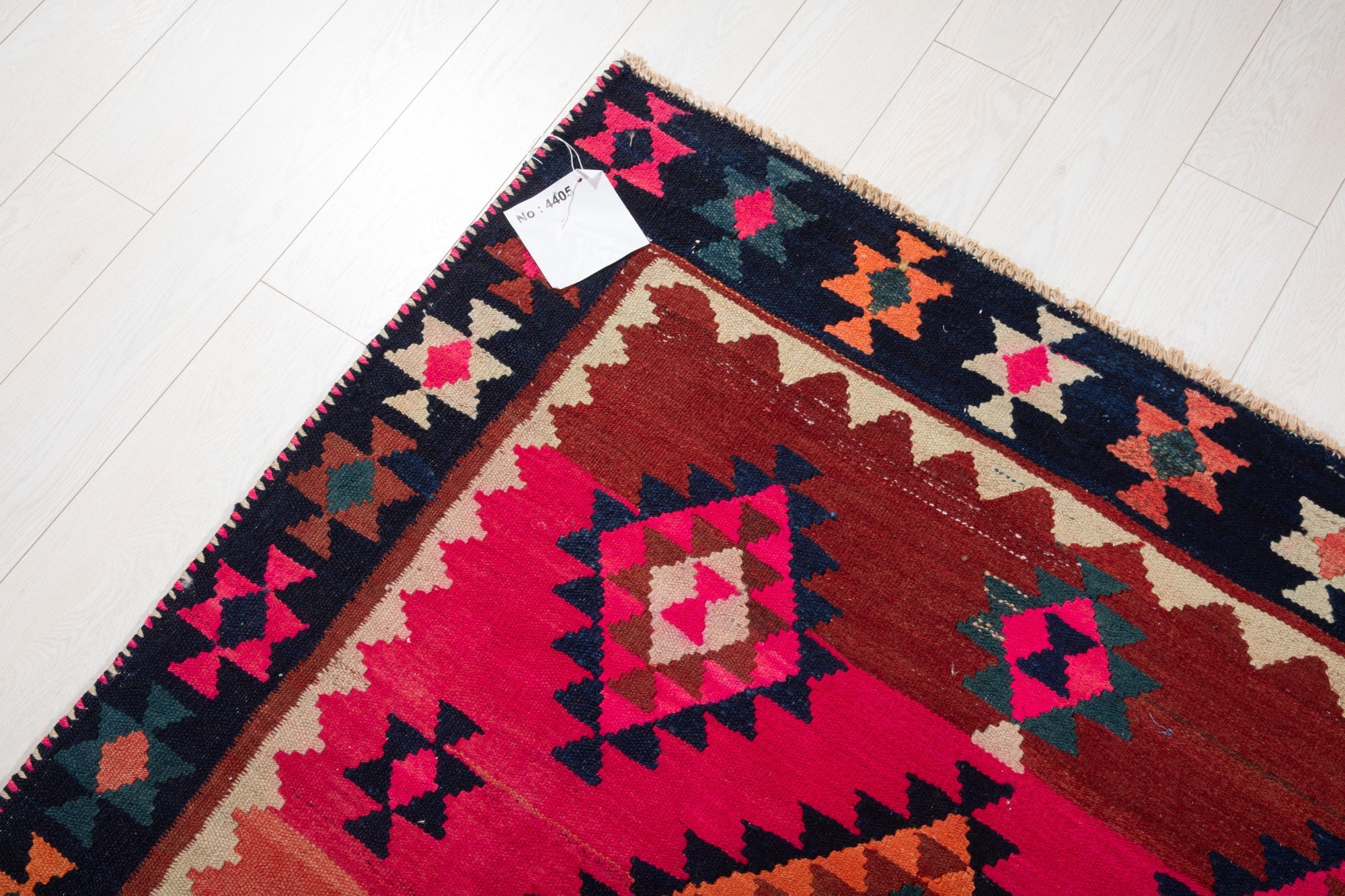 Corner of the vintage Shiraz Persian kilim rug with an attached inventory identification tag.