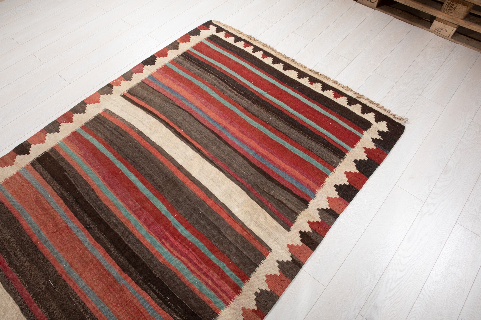 Warehouse angle shot of the striped kilim rug with pallets in the background.