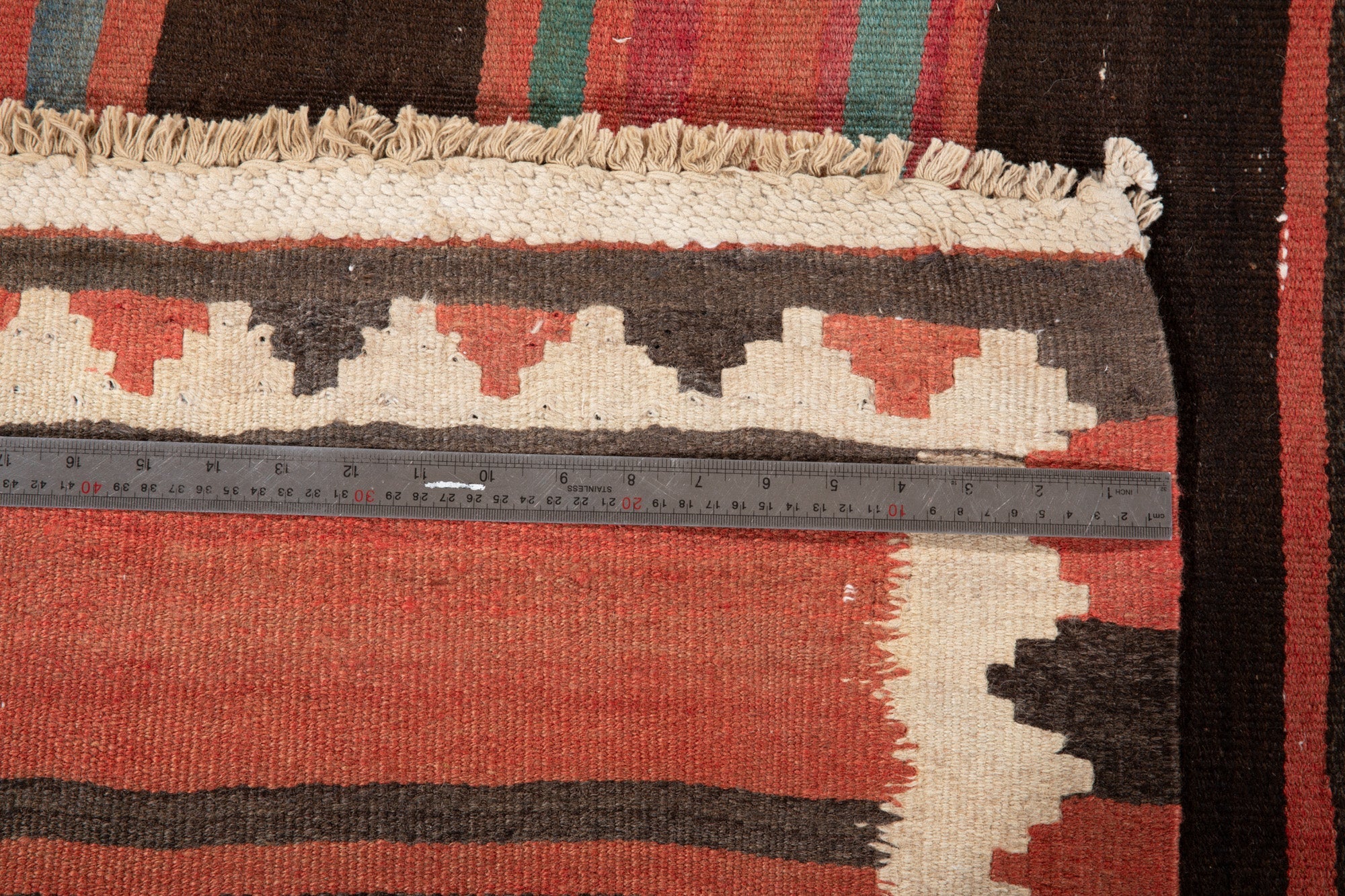 Ruler measuring the kilim's zigzag border width next to its fringe.