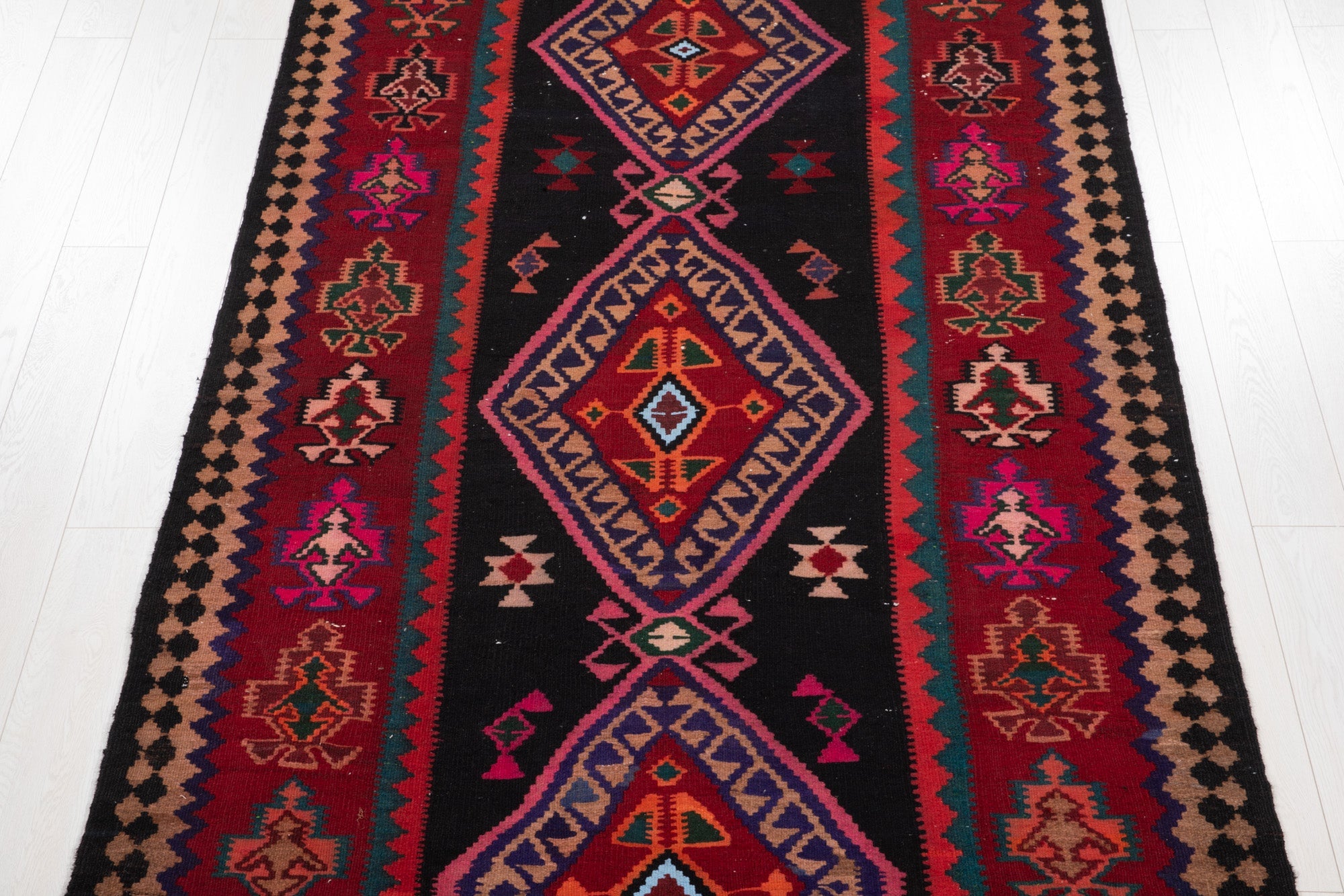 Top-down view of the kilim's diamond medallions on a black field with tree motifs.