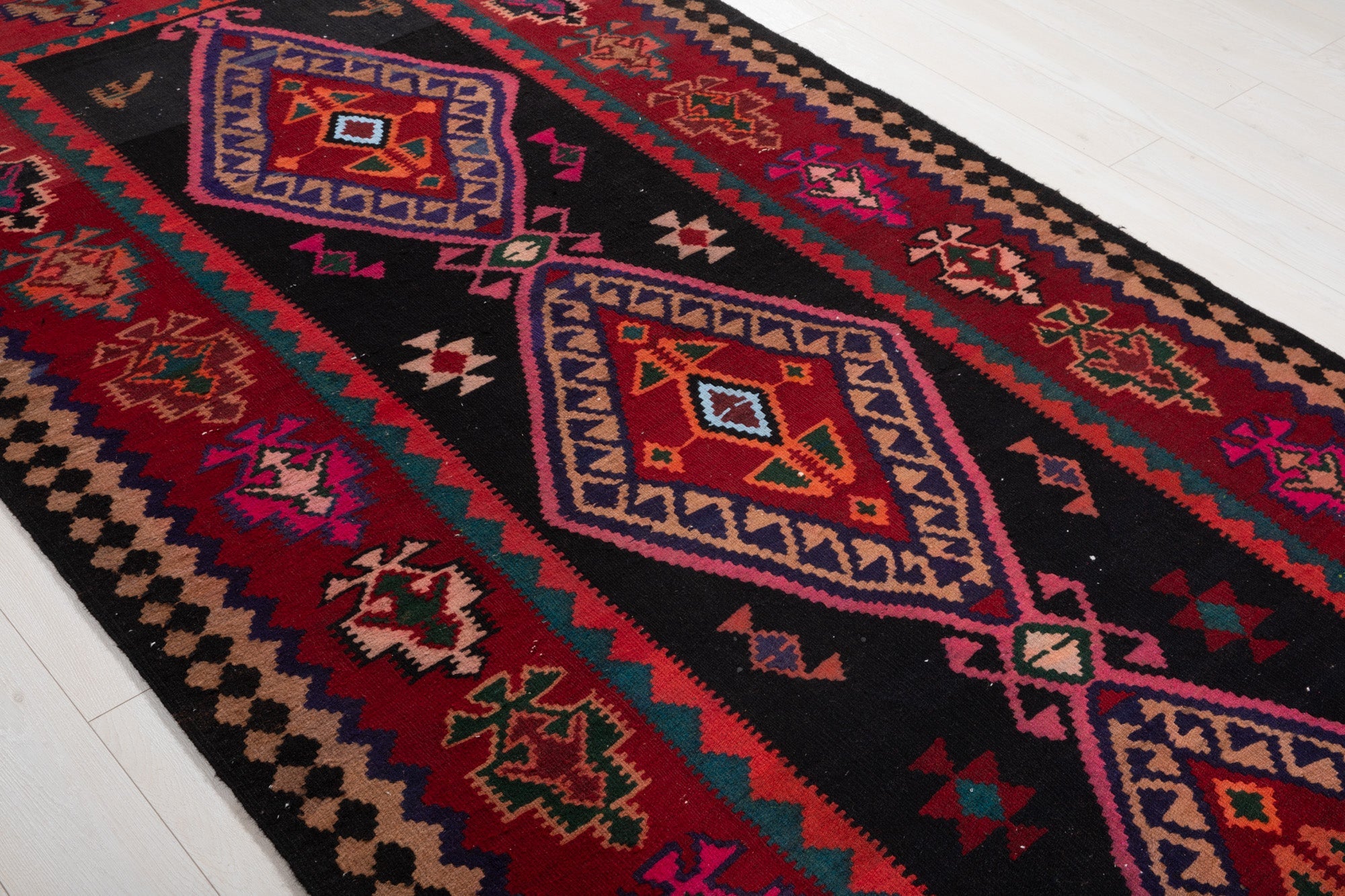 Diagonal close view of the kilim's diamond medallions and tree border motifs.