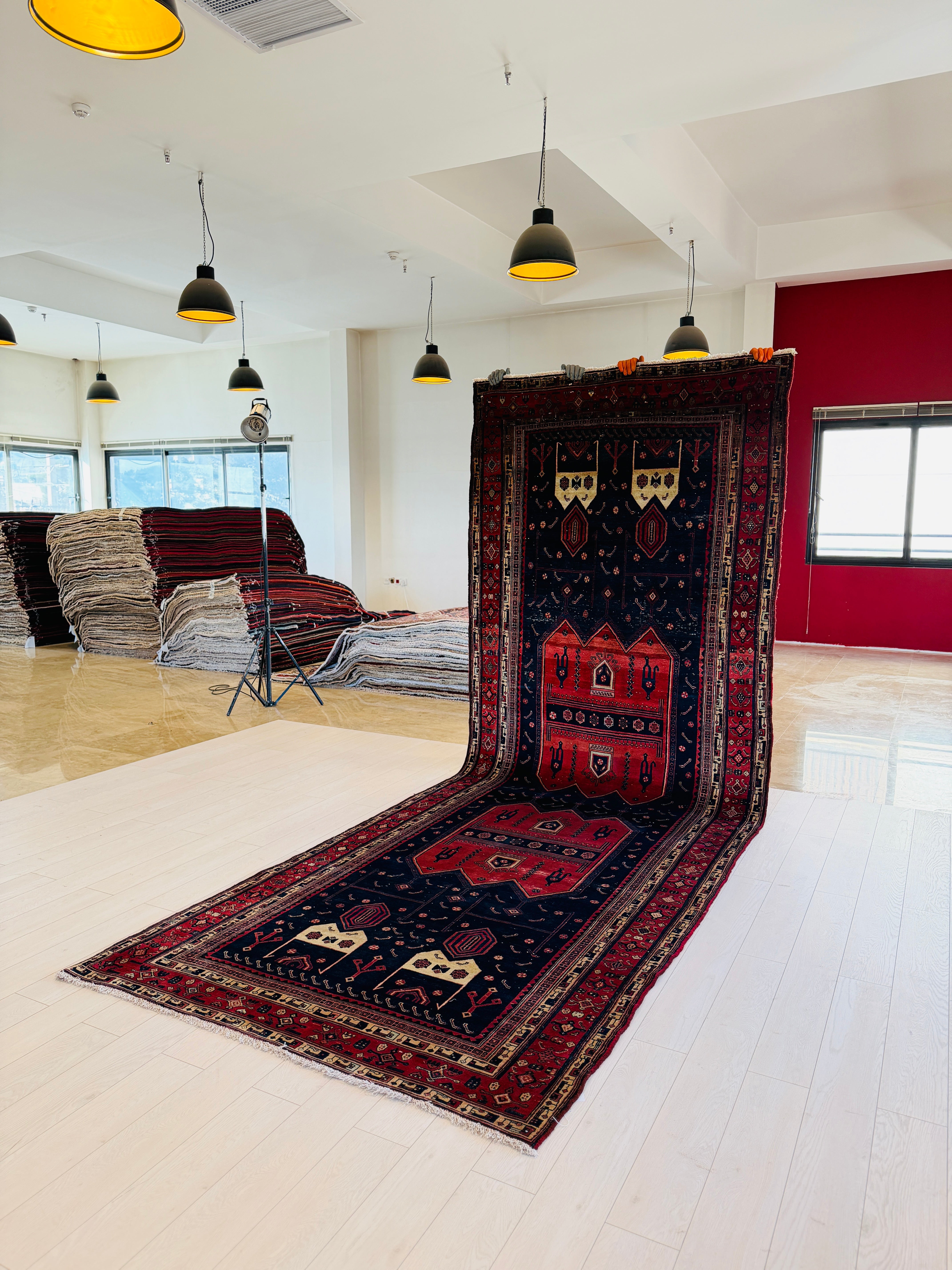 Kurdish Persian tribal rug hanging and unrolled in a showroom, displaying red and navy medallion pattern end to end.
