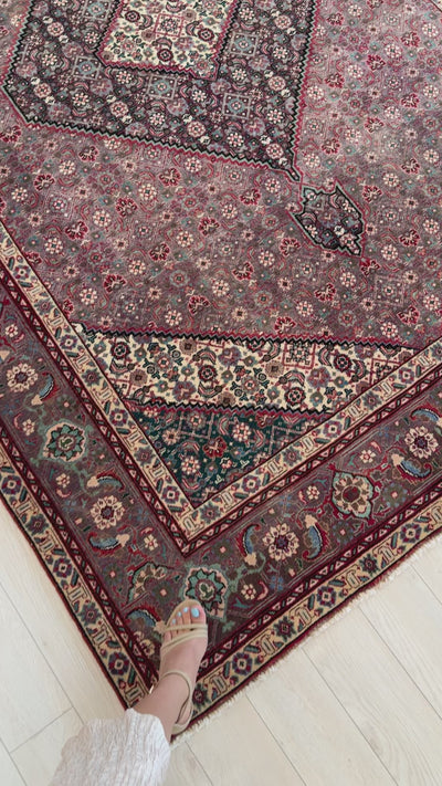 Corner detail of hand-knotted vintage Persian wool area rug featuring ornate border and vibrant floral motifs in red, green, and ivory.