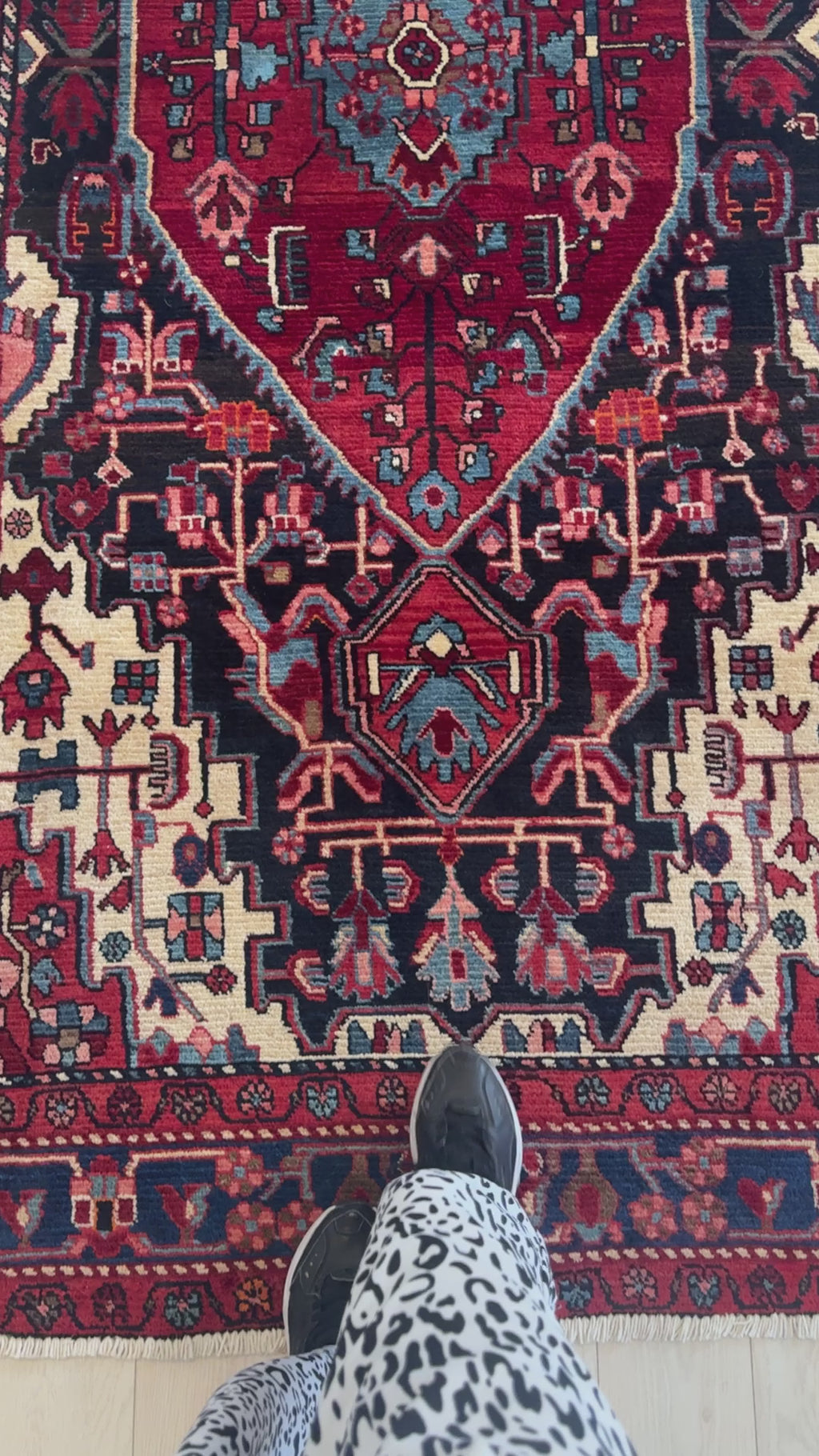 Close-up of Hand-Knotted Vintage Wool Area Rug – 9' 1 x 5' 1 showing detailed motifs and rich red, blue, and ivory color palette with feet for scale.