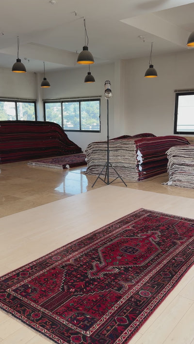 Hand-knotted vintage wool rug 9' 8" x 4' 6" displayed in a showroom with natural lighting, emphasizing its deep red and black motifs.