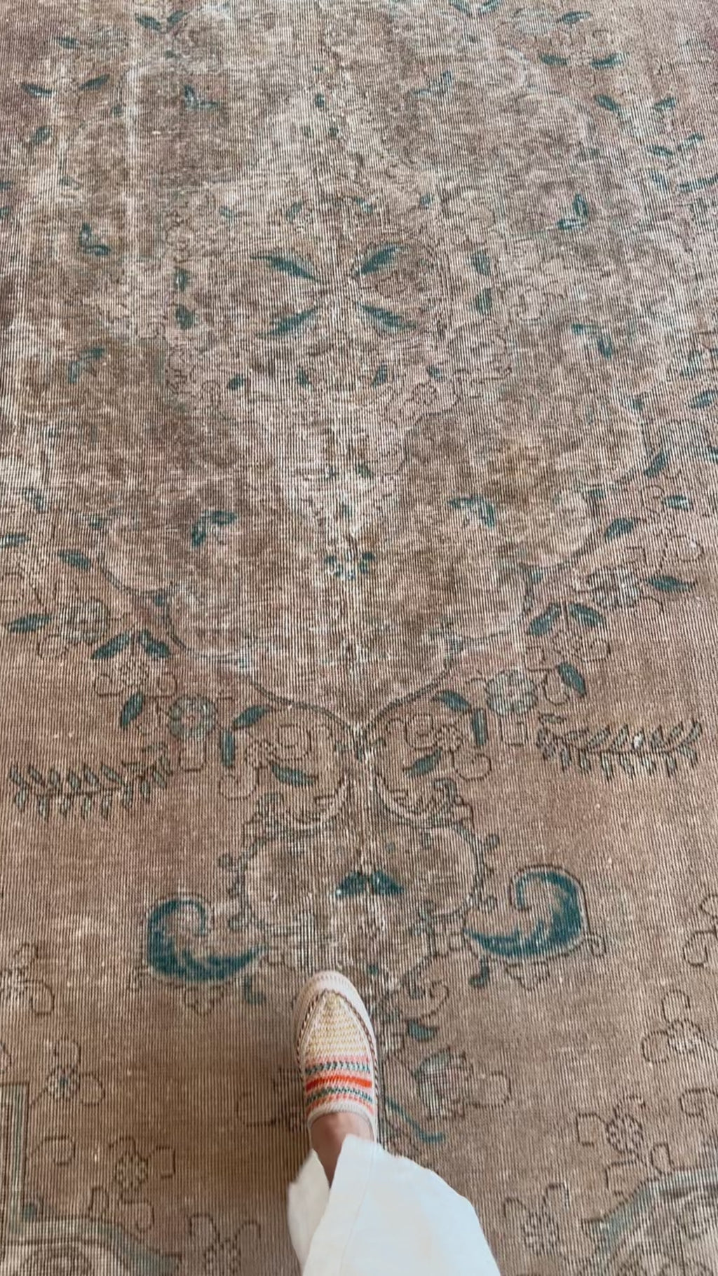 Close-up of hand-knotted vintage wool rug showing intricate faded floral patterns in teal and beige underfoot.