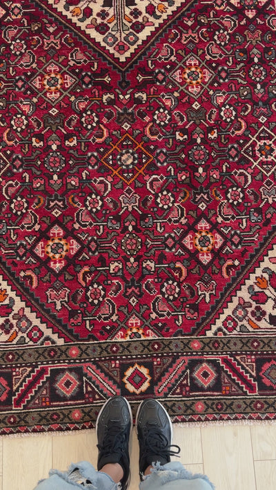 Close-up of Hand-Knotted Vintage Wool Area Rug – 10' 8" x 5' 2" showing detailed floral patterns and vibrant red hues underfoot.