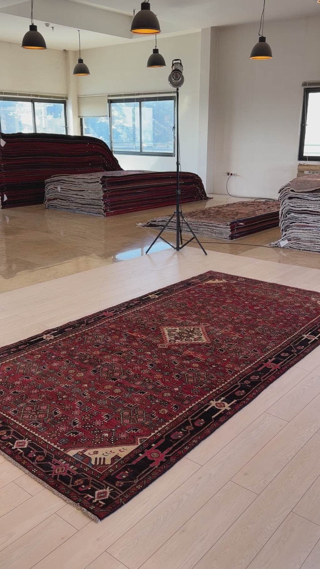 Hand-Knotted Vintage Wool Area Rug – 10' 11" x 5' 7" displayed in a showroom with stacked rugs, highlighting its bold red and black design.