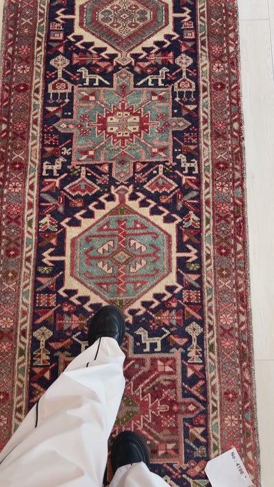 Detailed view of vintage wool runner rug 10' 9" x 2' 10" with tribal medallions and person standing on it for size reference.