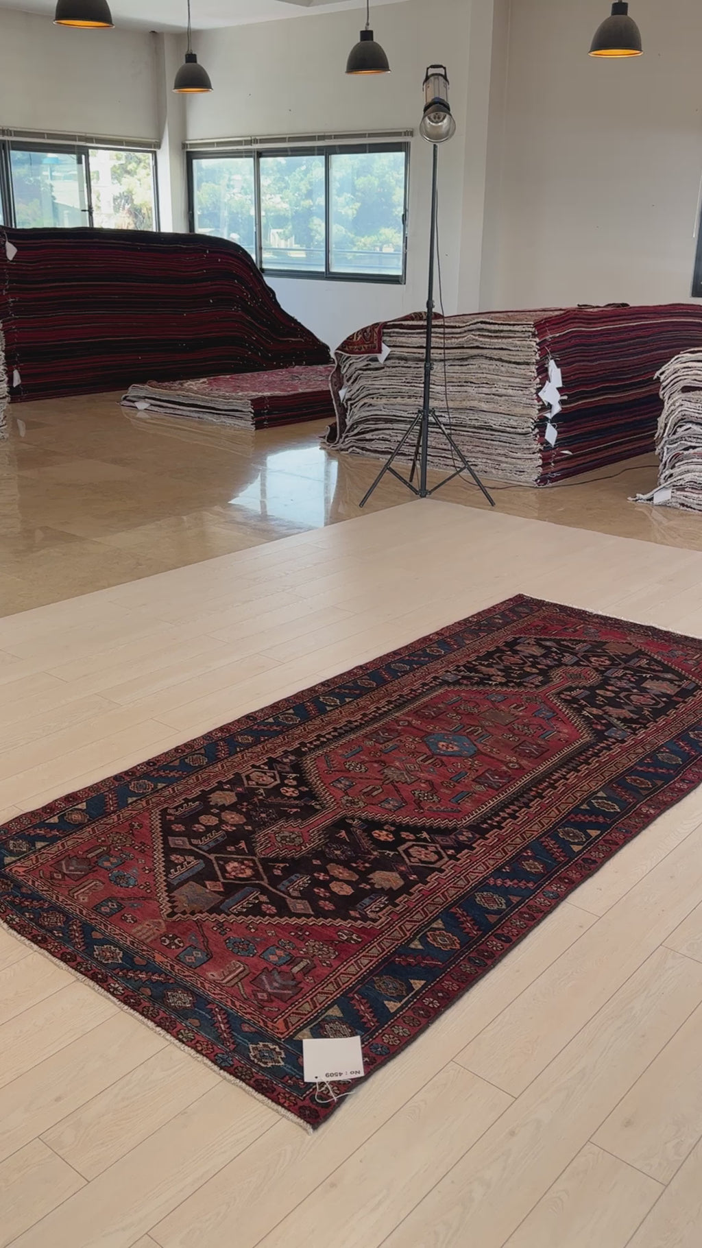 Hand-knotted vintage wool rug laid flat in a showroom, featuring a central medallion and intricate border in earthy red and navy hues.