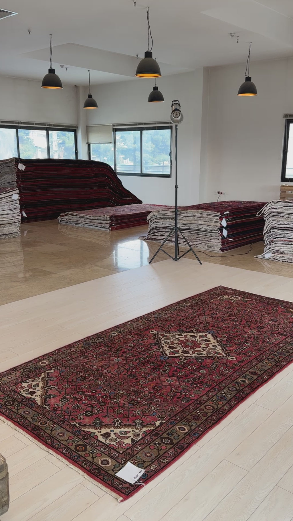 Hand-Knotted Vintage Wool Area Rug – 10' 8" x 5' 1" laid out in a showroom with stacks of rugs in the background, highlighting its rich red tones.