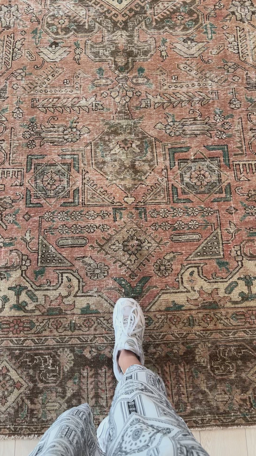 Close-up of foot on hand-knotted antique Persian Tabriz rug highlighting the intricate faded patterns and soft wool texture.