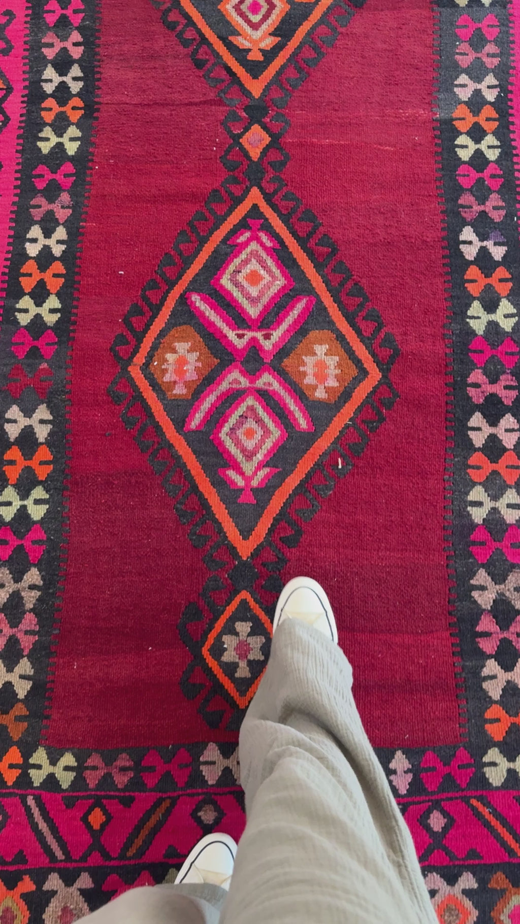 Close-up of a person walking on the Handwoven Vintage Wool Kilim Rug – 13' 3" x 5' 7", emphasizing the intricate diamond-shaped patterns and rich red hues.