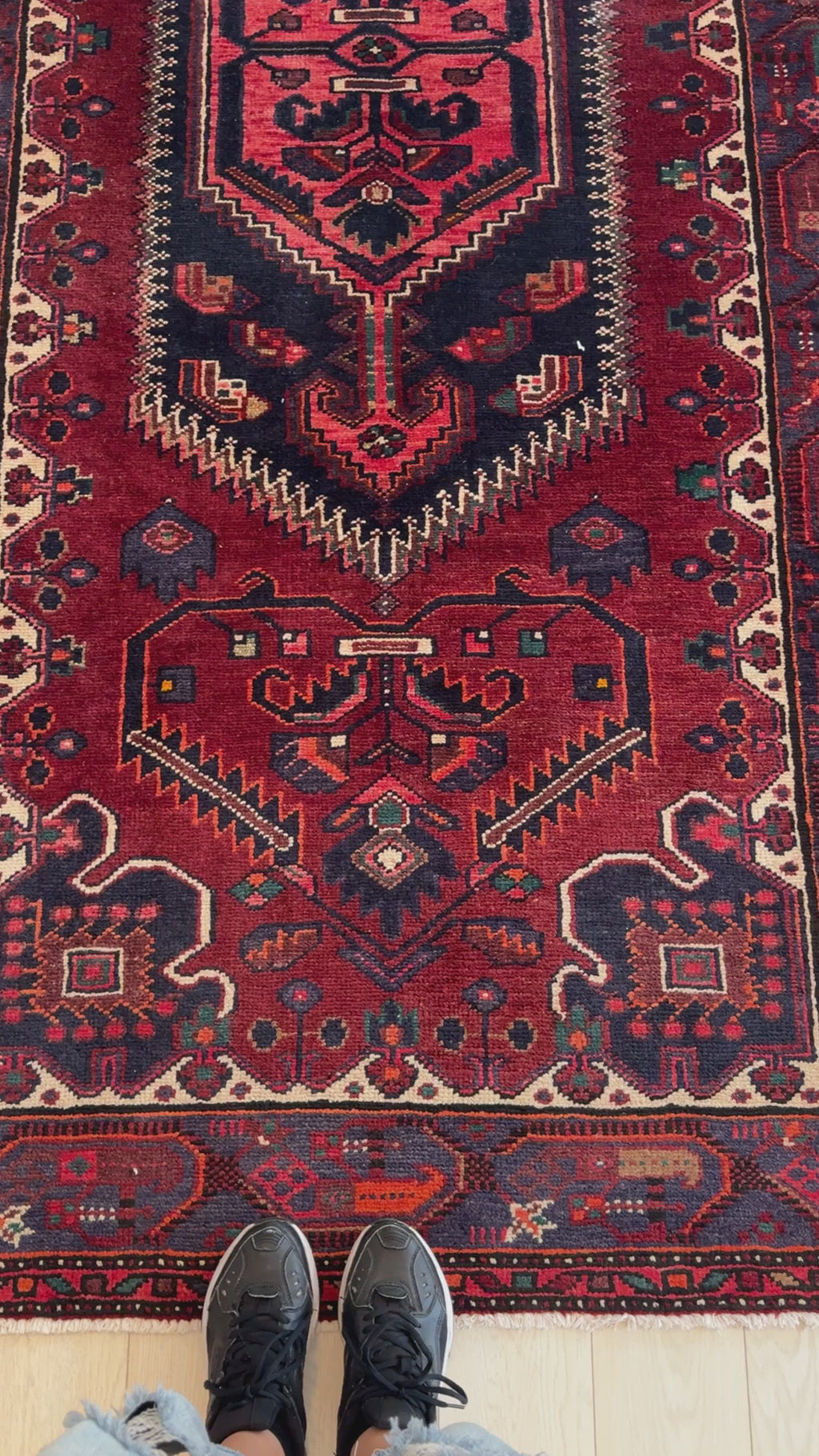 Close-up of Hand-Knotted Vintage Wool Area Rug 9' 4" x 4' 5" showing intricate tribal patterns and rich red hues with shoes for scale.