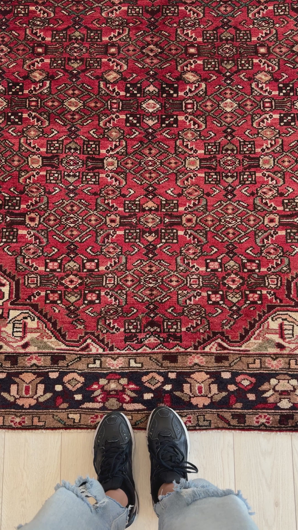 Close-up view of hand-knotted vintage wool area rug 10' 6" x 5' 5" showing detailed red and black geometric patterns underfoot.