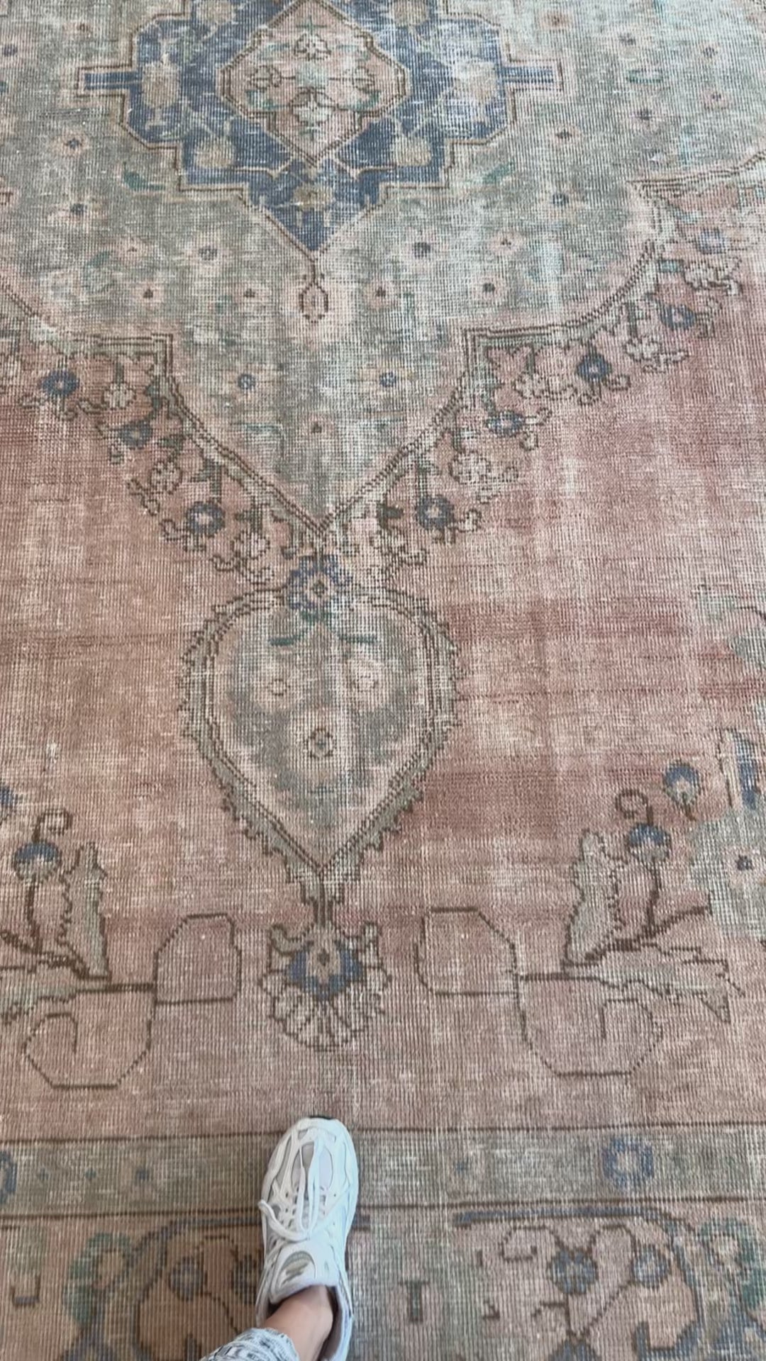 Close-up of hand-knotted Tabriz vintage wool rug showing intricate faded floral patterns and texture underfoot.